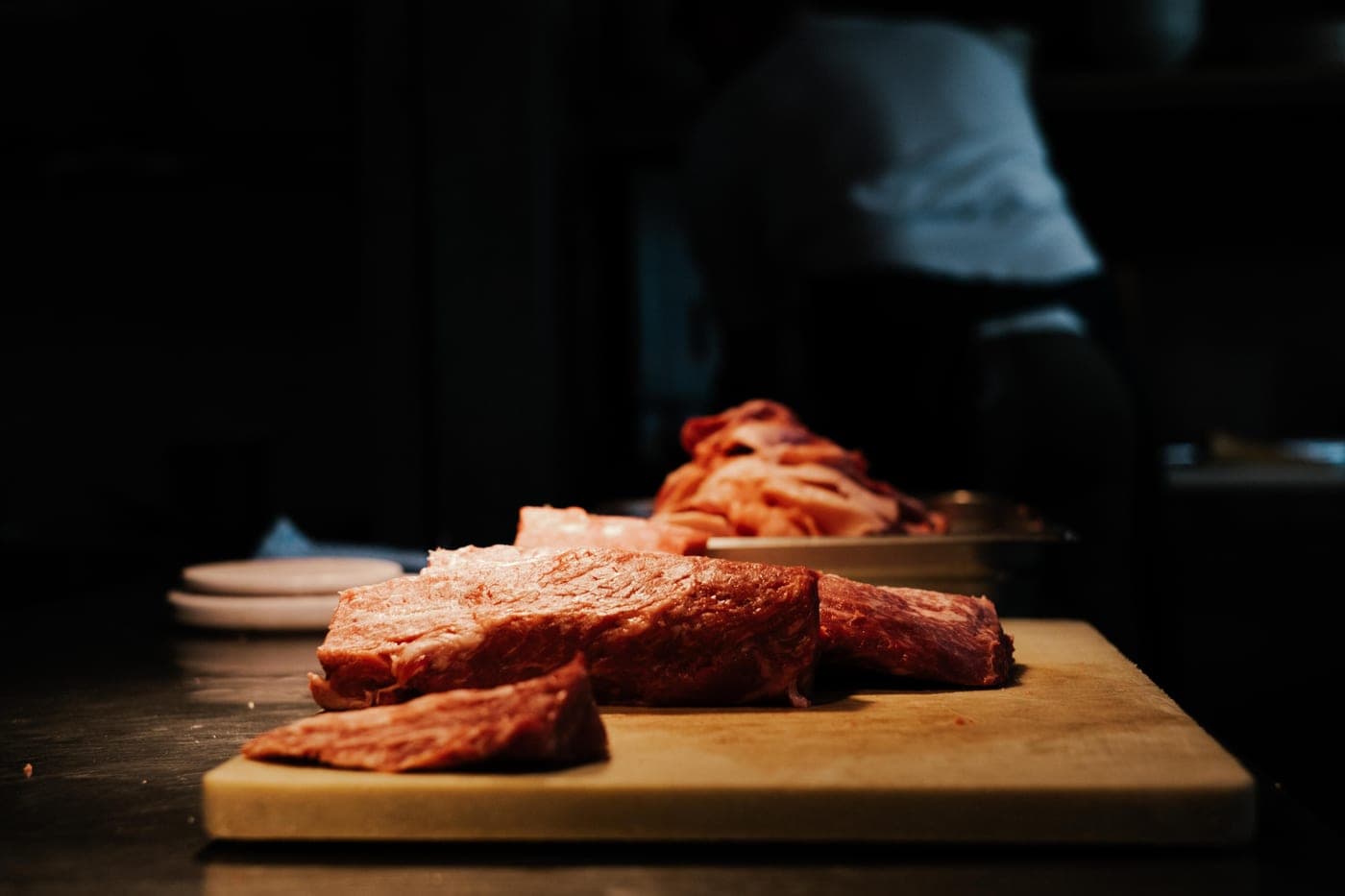 Cuts of raw meat on a wooden cutting board in a dim butcher's kitchen
